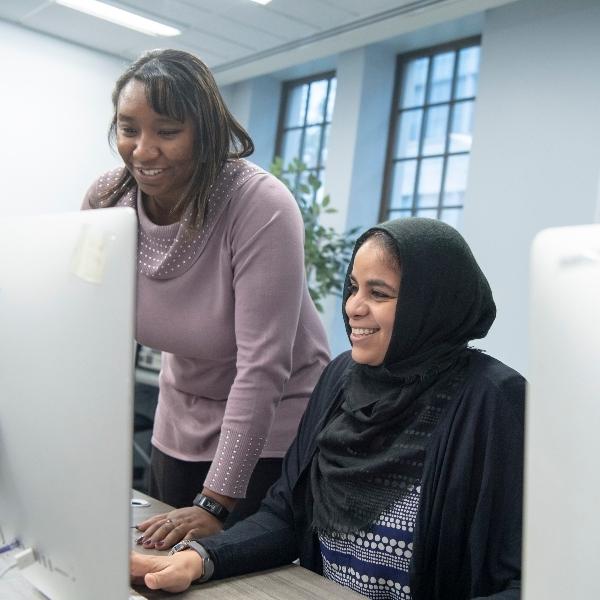 Two digital media graduate students looking at a computer screen and smiling.